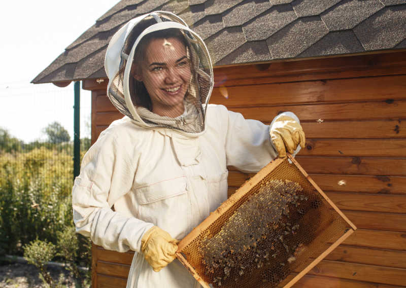 W lady in a beekeeping suit next to a beehive