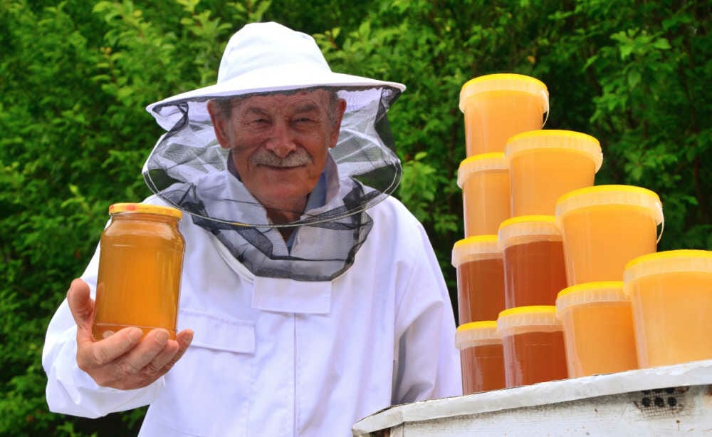 A beekeeper holding a large jar of honey in his beekeeping suit.