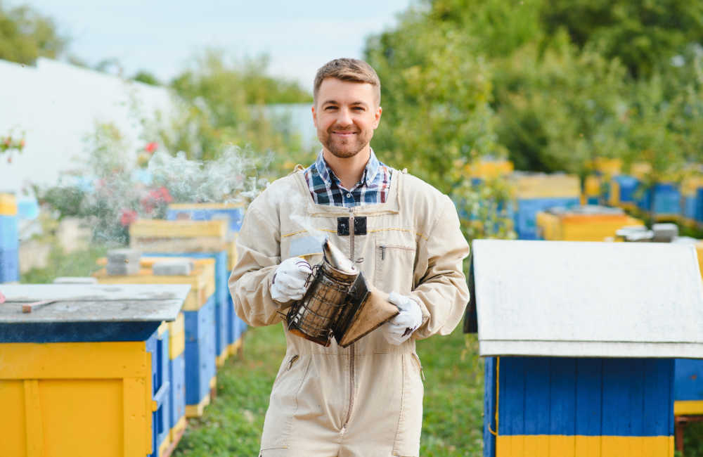 A beekeeper holding a smoker next to some hives