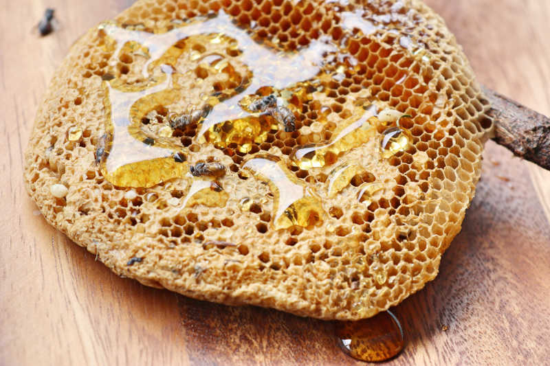 Honey comb with liquid honey seeping out on a wooden board