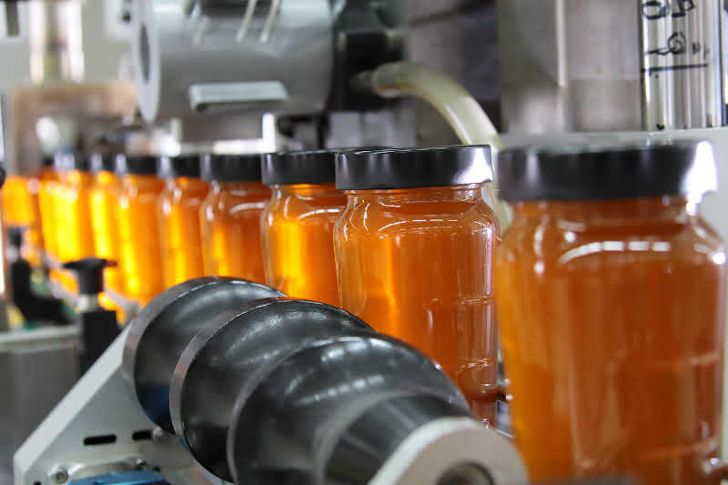 A long row of freshly jarred honey in a honey room