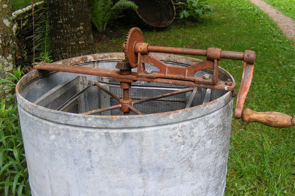 A vintage honey extractor with lawn in the background